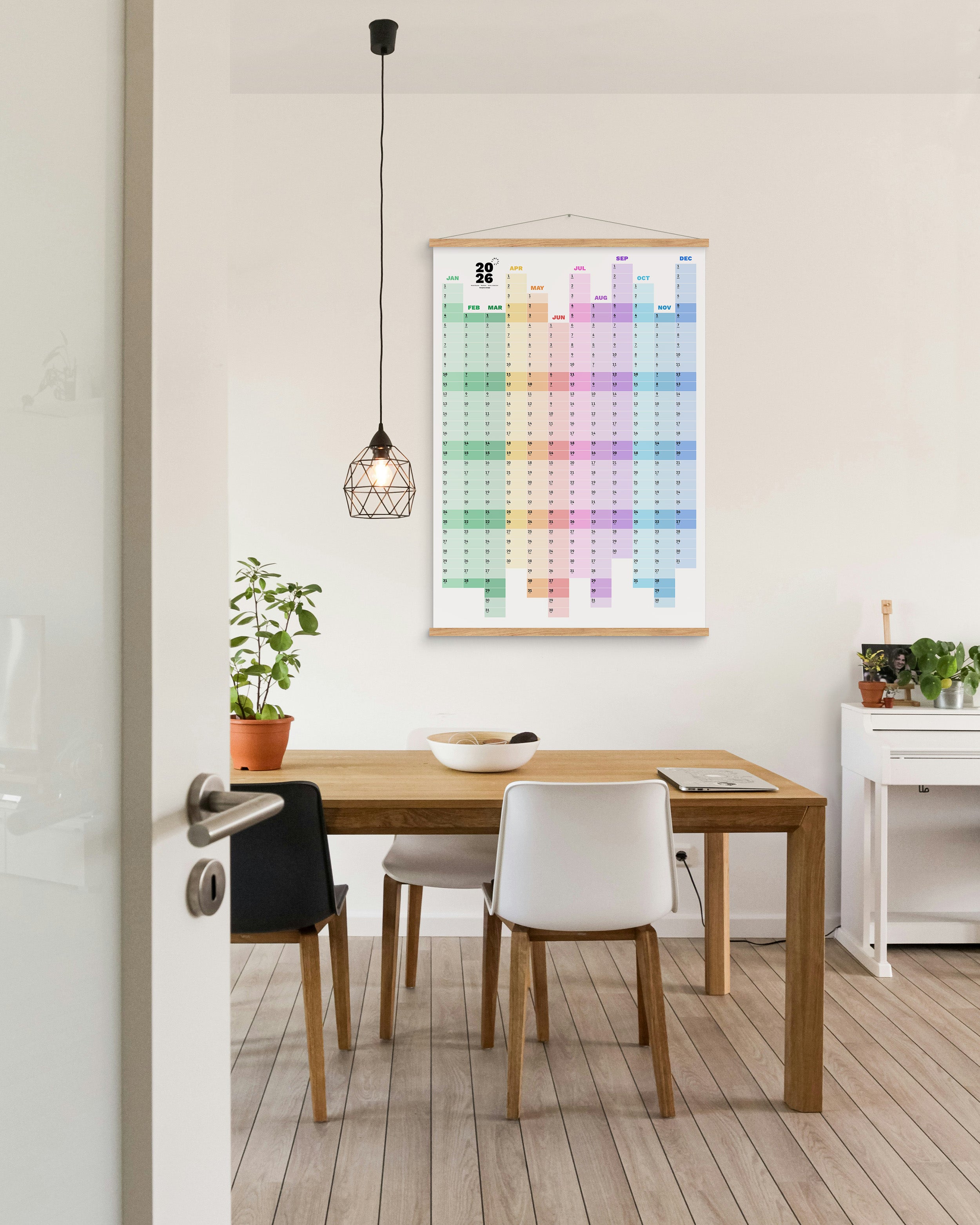 Colourful wall calendar in a dining room setting with a wooden desk and chairs.