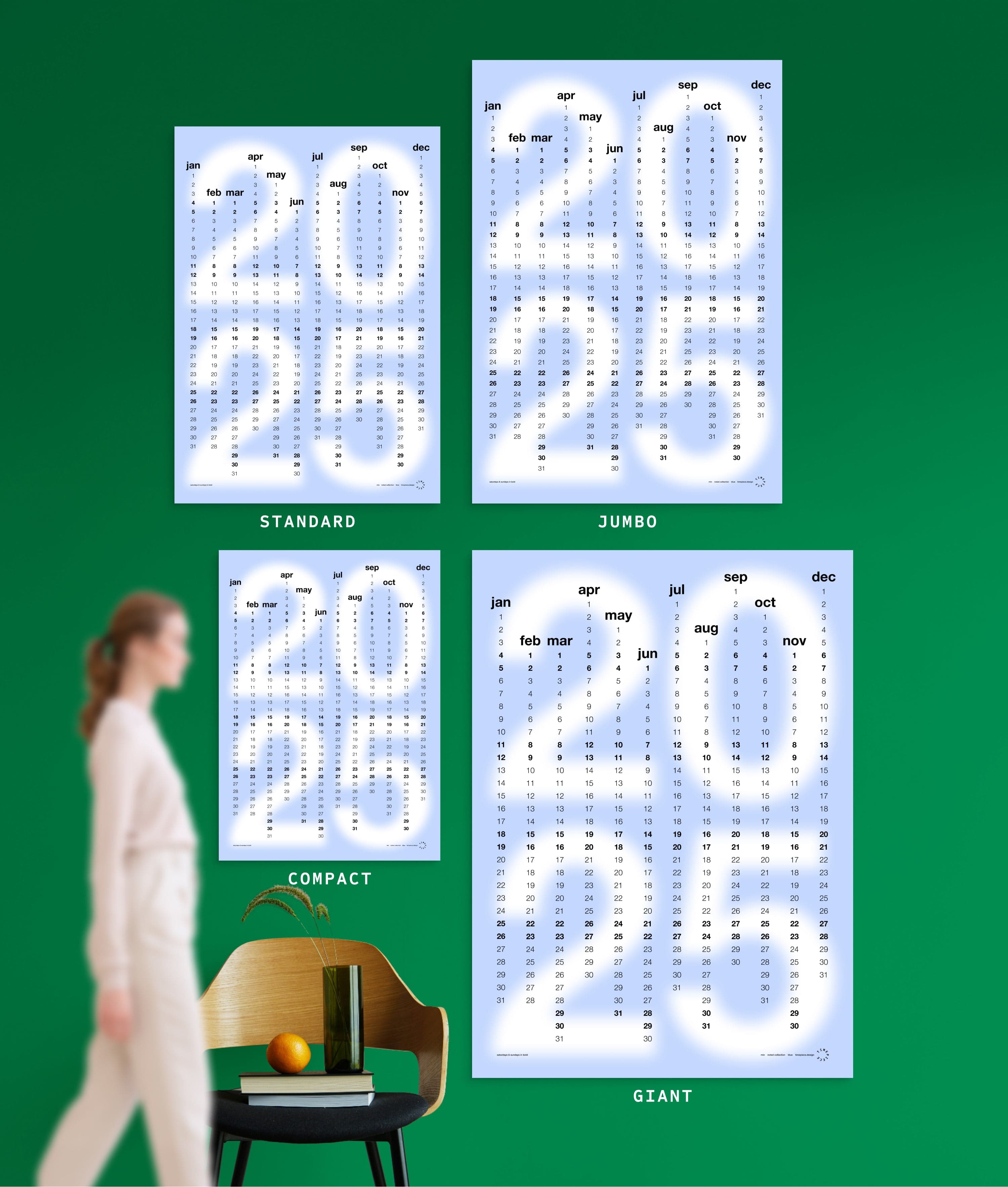 4 sizes of Min in Blue colour yearly planner on green wall, with person, chair, orange and vase shown for scale