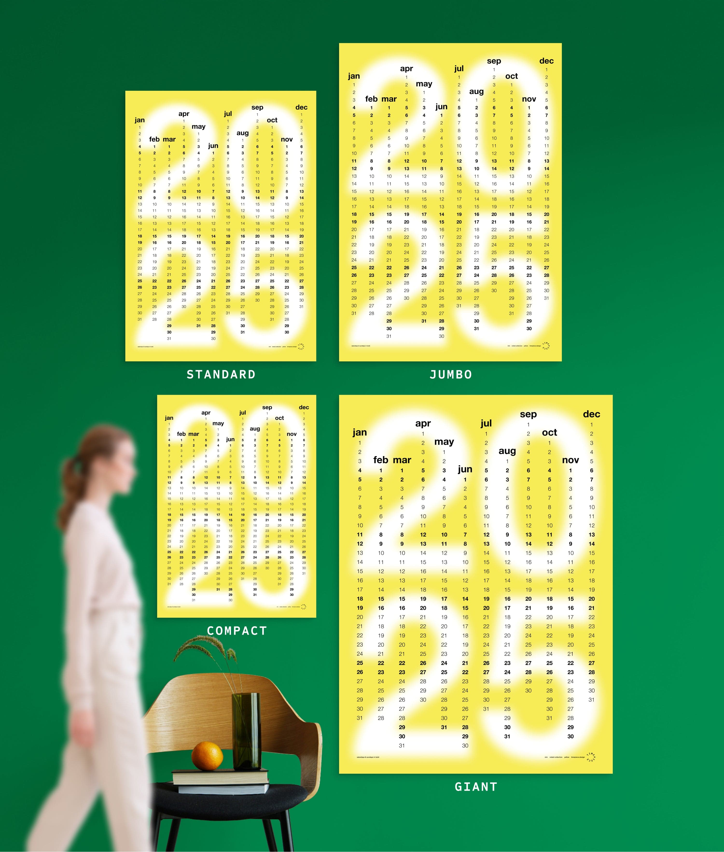 4 sizes of Min in Yellow colour yearly planner on green wall, with person, chair, orange and vase shown for scale